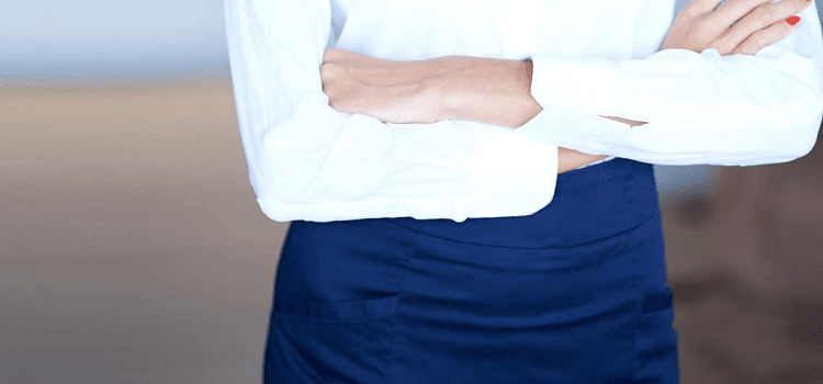 woman wearing a navy skirt and white blouse with her arms folded; photo is cropped so no tights are shown.