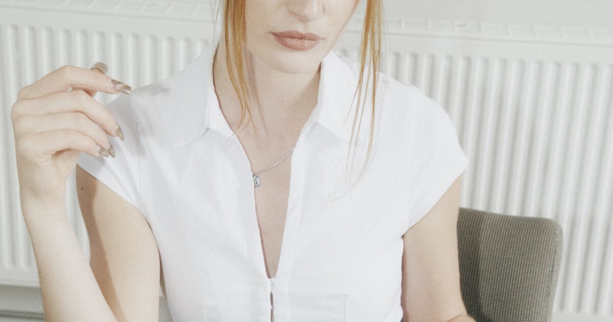 professional woman wears white top for spring with her work outfit; she is drinking an espresso and looking somewhat bored