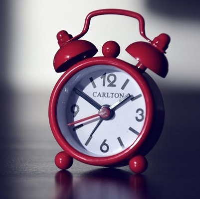 red alarm clock sits on a table; shadows are in the background