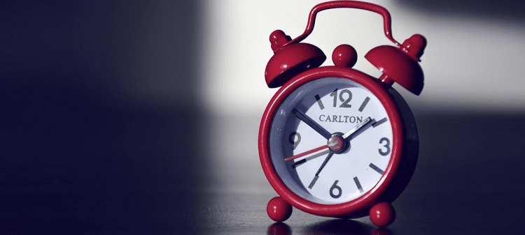 red alarm clock sits on a table; shadows are in the background