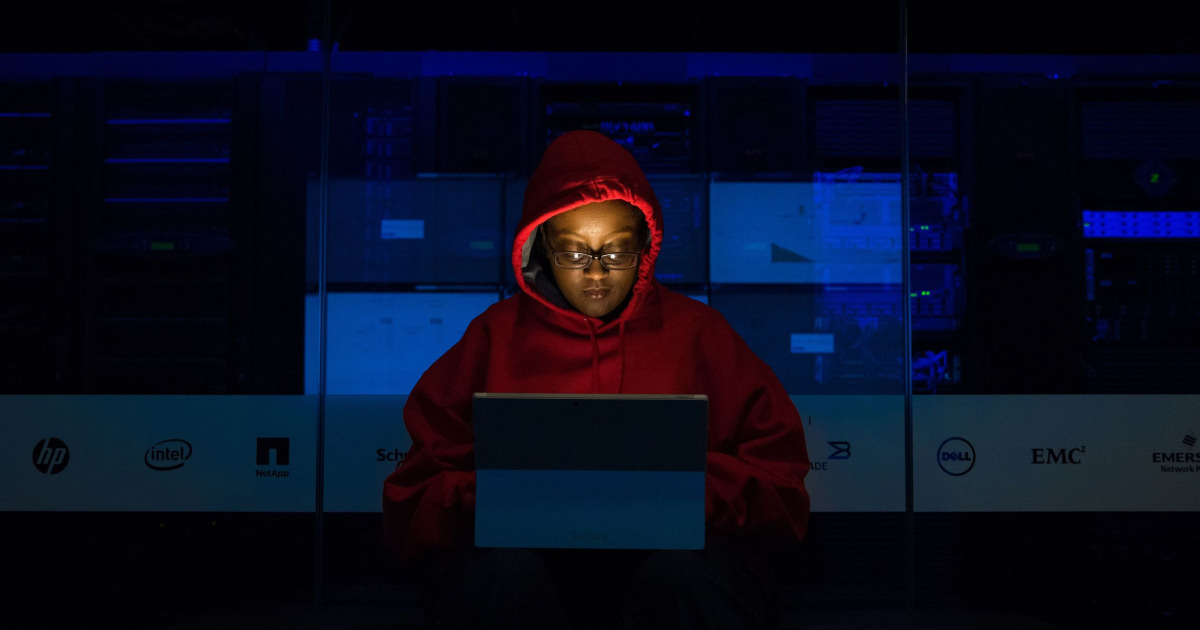 a woman in a red hoodie works in a dark office at a computer