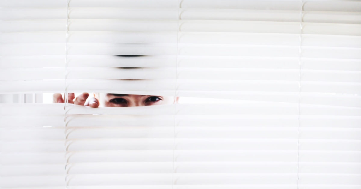 woman peeking through white blinds