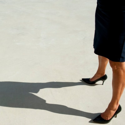 tall professional woman standing in heels and pencil skirt looking at her long shadow