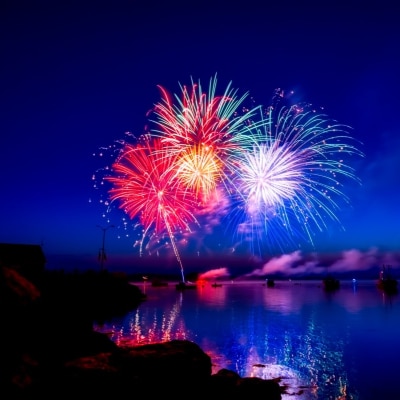 colorful fireworks explode over water, against a dark sky
