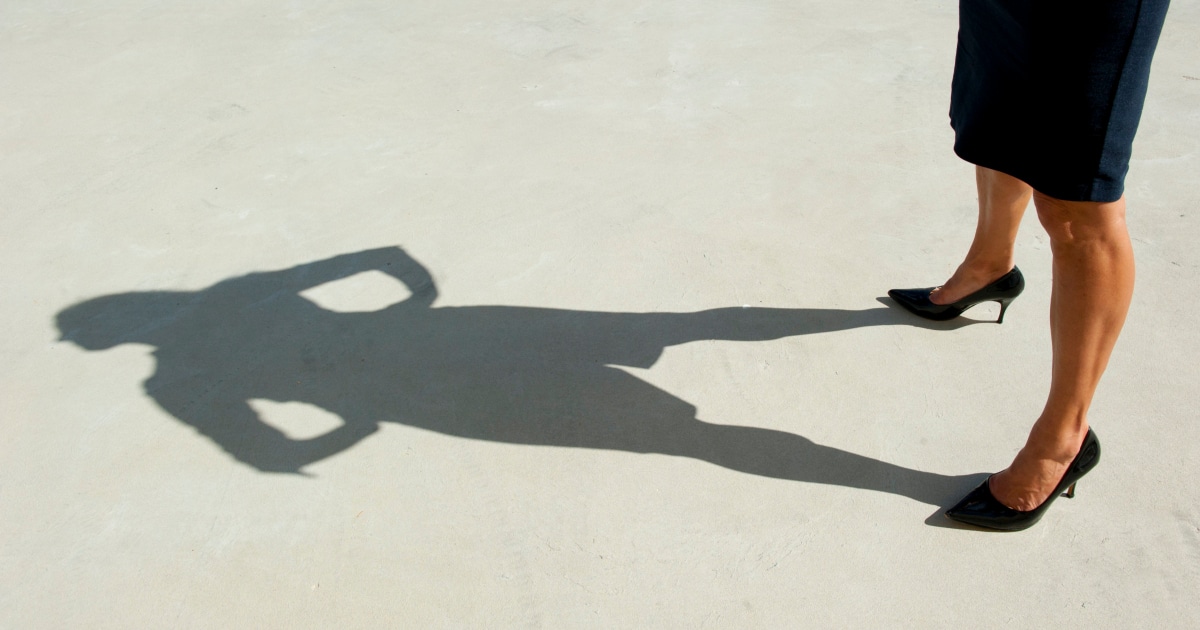 tall professional woman standing in heels and pencil skirt looking at her long shadow 