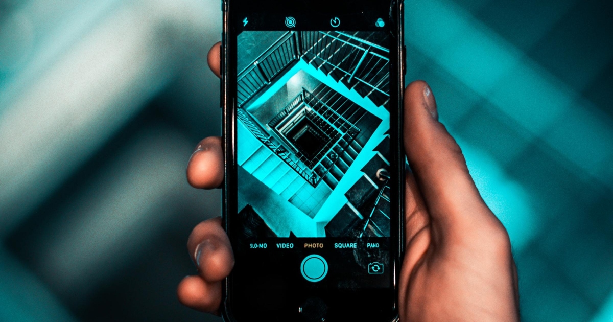 woman using iPhone camera to take a photo of a green-lit staircase well