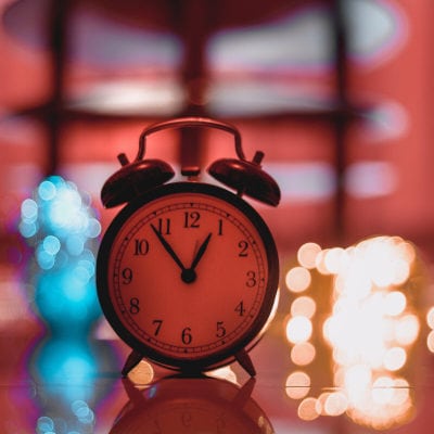 analog alarm clock in a dark room with out of focus lights behind it