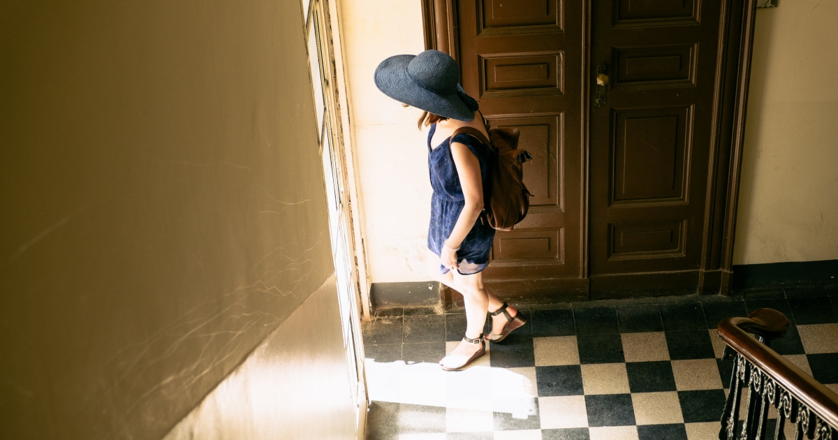young professional woman wearing backpack and sunhat walking out door in Turin hotel