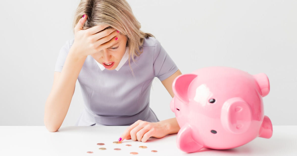 frustrated young professional woman counting pennies near a pink piggybank