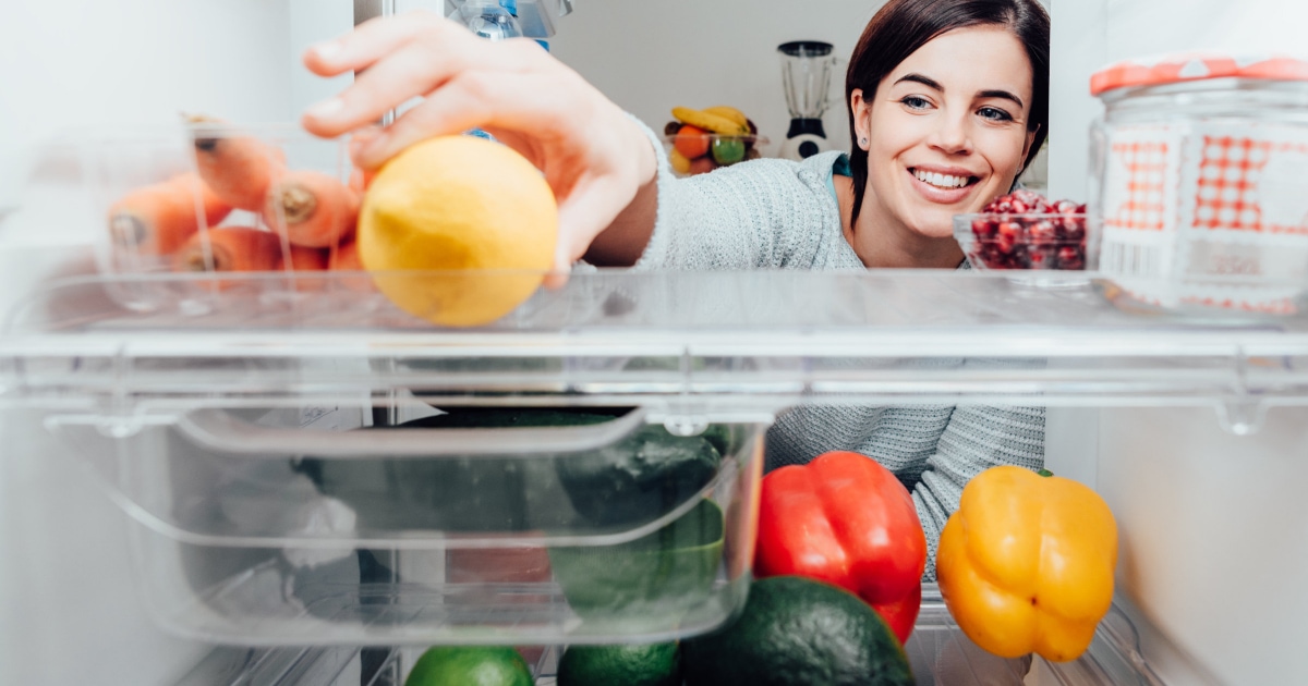professional young woman peering into clean, organized fridge