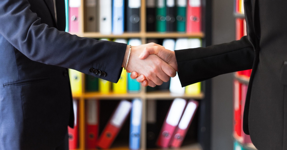 two businesspeople shaking hands in front of binders