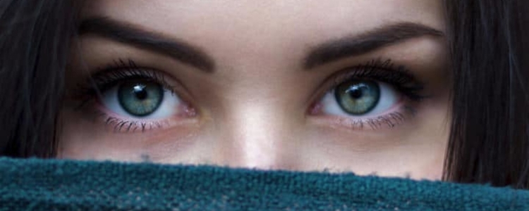 close-up of woman's greenish eyes; she has brown hair and is covering the lower part of her face with a teal turtleneck, scarf or blanket