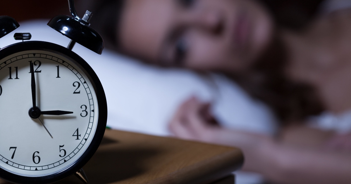 woman lying awake looking at an alarm clock reading 3AM