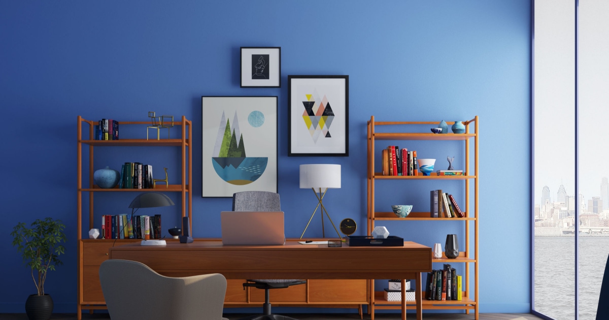 view of home office with blue walls, bookshelves, desk, artwork, lighting and more