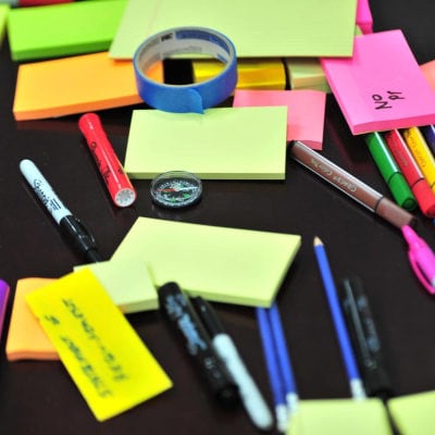 office supplies such as neon post-its, pens, and more spread across a black desk