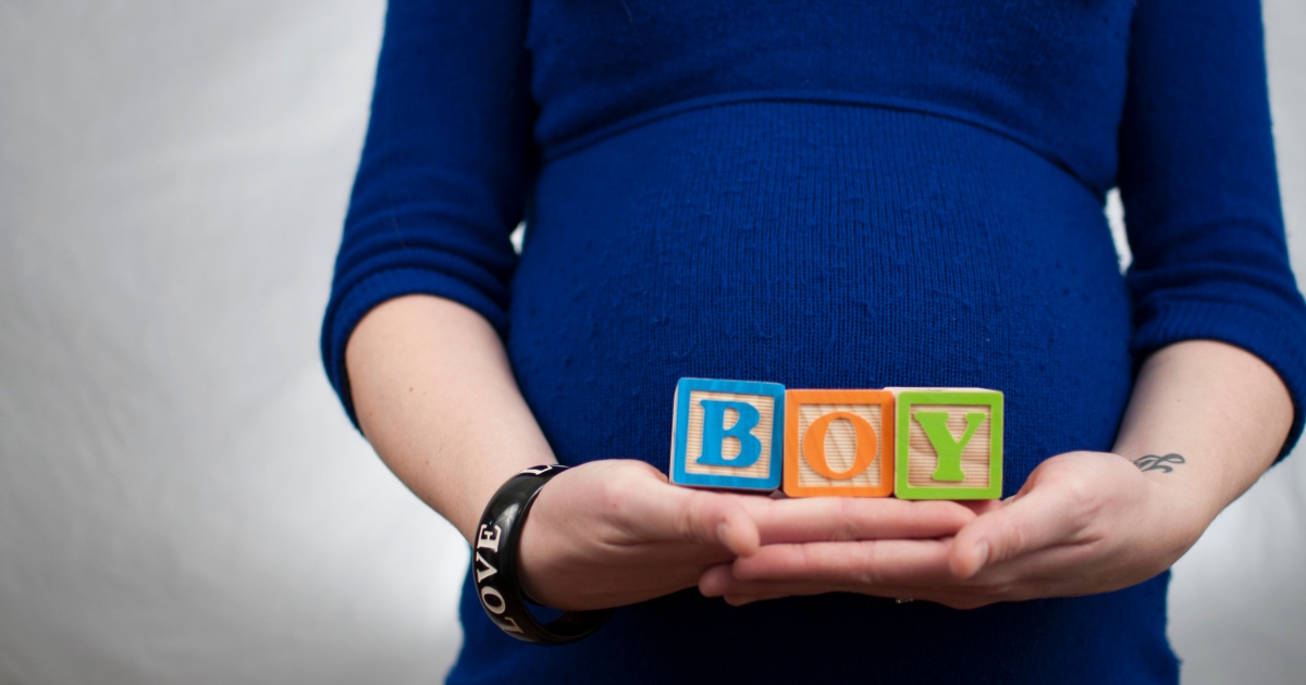 young professional pregnant woman wearing a blue maternity dress and holding toy block letters reading B O Y