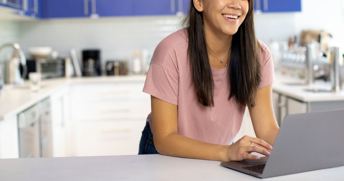 young professional woman works on computer from her kitchen at home