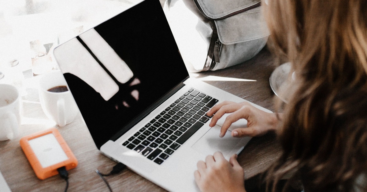 woman works on laptop; there is an orange cell phone charger in view as well