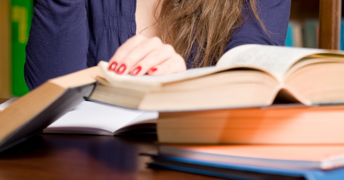 female law student pages through law textbooks; she has red nails