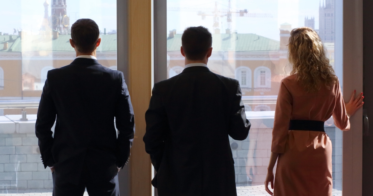 professional woman standing at window looking out with men in suits