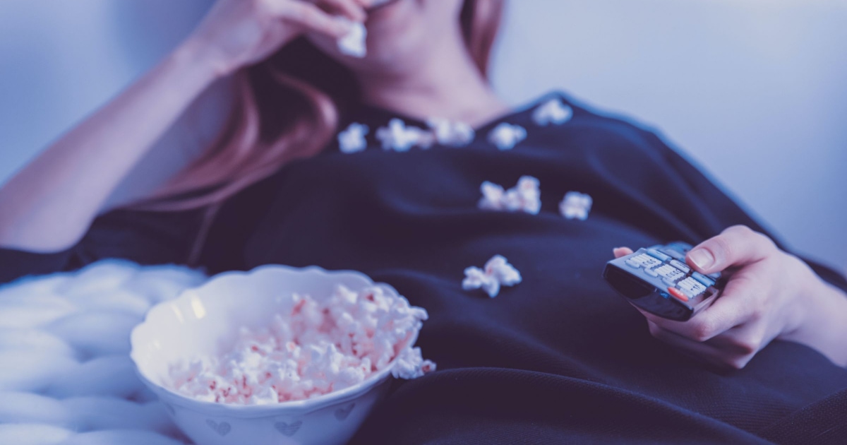 woman slouches on couch, eating popcorn