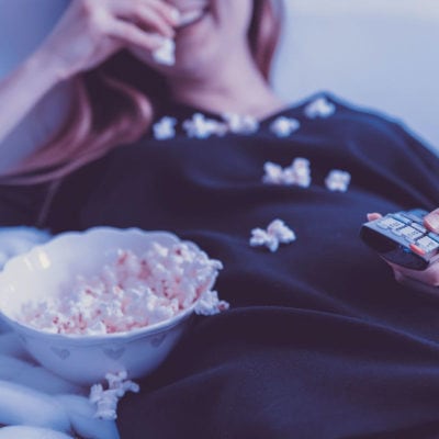woman slouches on couch, eating popcorn