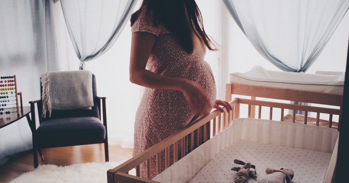 young woman wearing a pink dress standing over crib