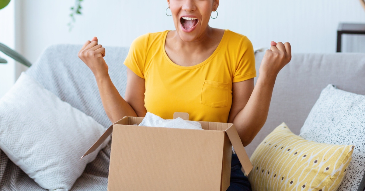 young professional black woman in a yellow t-shirt really excited about a package