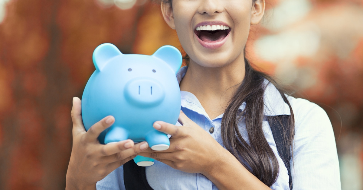 personal finance tasks to do asap in a new year professional young woman smiling while holding a blue piggy bank