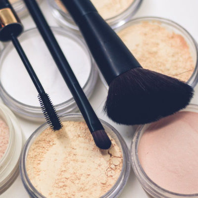 uncapped pots of blush and powder with makeup brushes sitting on top