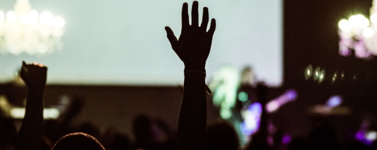 a few hands raised at a conference with lights, screen and people blurry