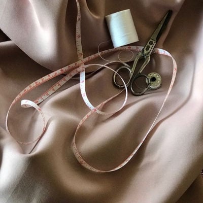 alteration supplies such as scissors, thread and measuring tape on top of beige satin