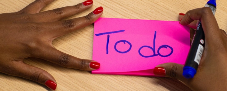 black woman with red fingernails writing on a pink Post-it note 