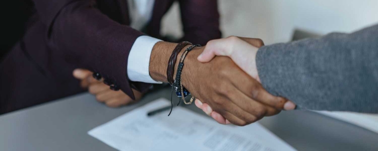 white woman in gray blazer shaking hands with a black man in a purple suit