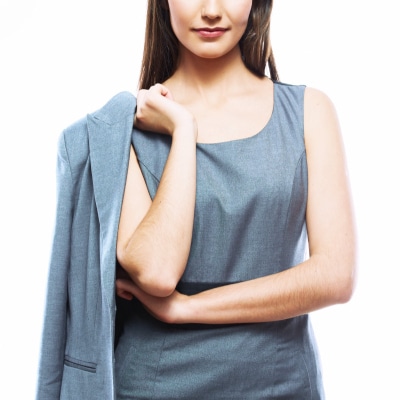 young professional woman wears a sheath dress in a suiting material; her suit blazer is thrown over her shoulder