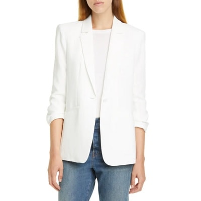 A white woman (face partially cropped out) wearing a white blazer, white shirt, and jeans 