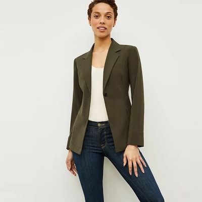 A Black or biracial woman with short hair wearing a white shirt under a olive-colored blazer and jeans