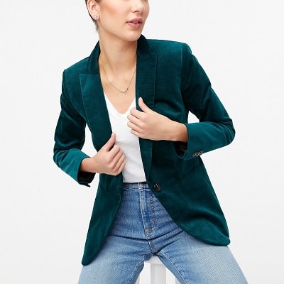 A light-skinned woman (head partially cropped out) wearing a green velveteen blazer, white shirt, and jeans 