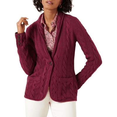 woman in shawl-neck sweater jacket with thick cable knit and two patch pockets;  her sweater jacket is maroon, her collared blouse is pinkish underneath and she's wearing winter white pants