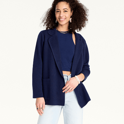 woman in a loose navy blue sweater blazer with notch collar, patch pockets, and no buttons; she wears a navy crop top beneath it and light blue denim jeans
