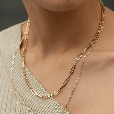 white woman wearing two gold link necklaces against a beige asymmetrical sweater