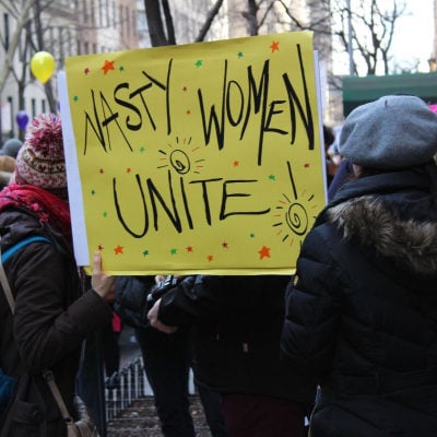 protest with yellow handwritten sign reading NASTY WOMEN, UNITE!