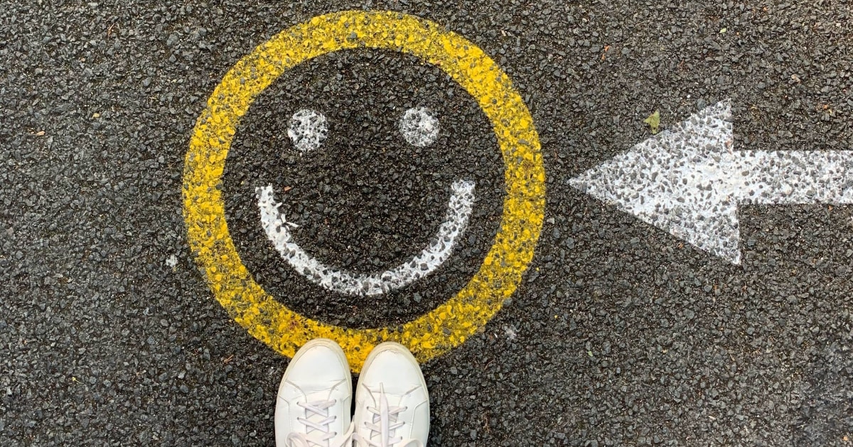 smiley face painted on gravel, woman in white sneakers standing over them