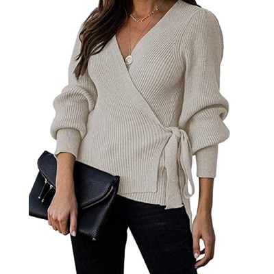 A white woman with long brown hair (face cropped out) wearing an off-white wrap sweater and black pants and carrying a black clutch