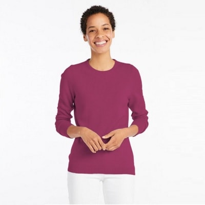 A Black woman with short natural hair wearing a pink sweater and white pants