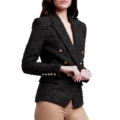A white woman with long brown hair (face partially cropped out) wearing an olive-colored blazer and tan pants (legs mostly cropped out)