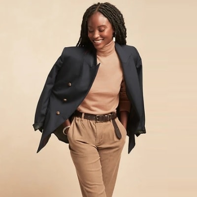A Black woman with braids wearing a navy blazer, camel-colored sweater, tan pants, and a brown belt