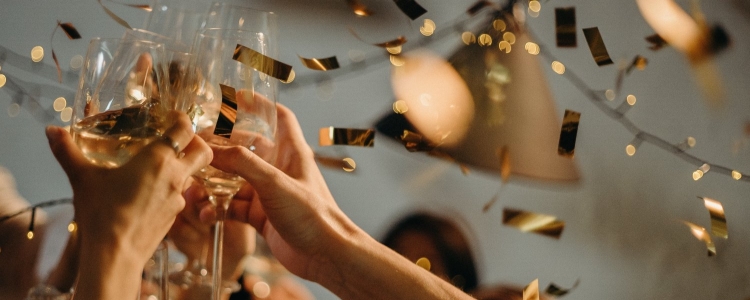 several hands raise champagne glasses as gold confetti floats in background; it's a great holiday office party