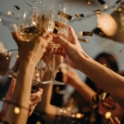 several hands raise champagne glasses as gold confetti floats in background; it's a great holiday office party