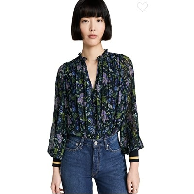 An Asian woman with short black hair in a bob haircut wearing a black floral shirt and jeans (legs mostly cropped out) 
